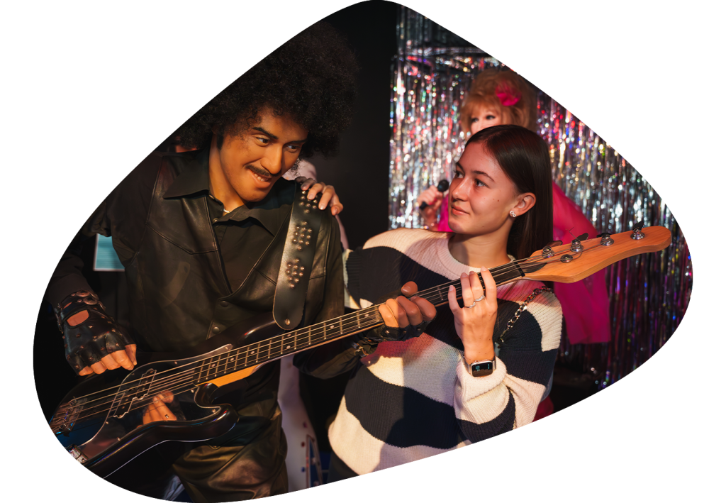 Girl pretending to play bass guitar with the musical wax figure